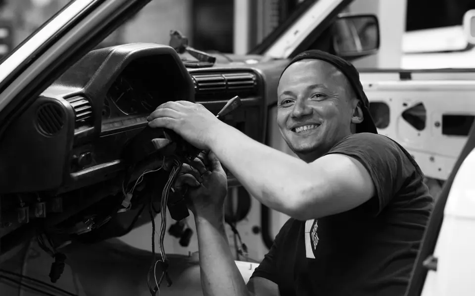 A mechanic working on wiring behind a car dashboard